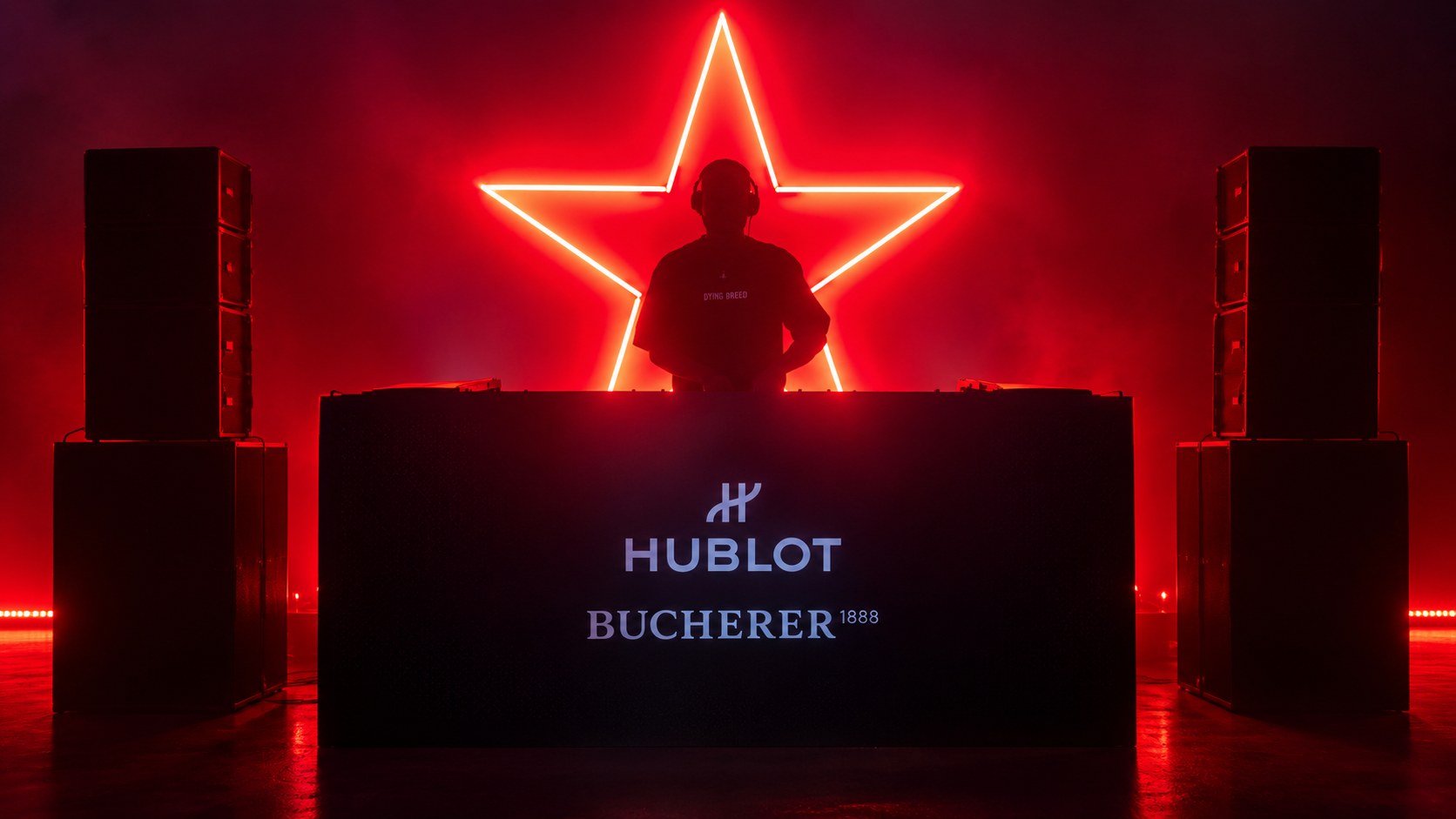 DJ silhouetted against a red neon star behind a booth branded Hublot and Bucherer