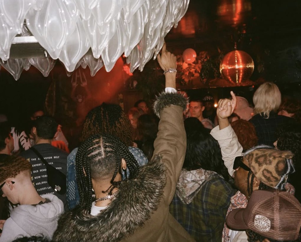A packed dance floor with hands in the air under a chandelier and disco ball